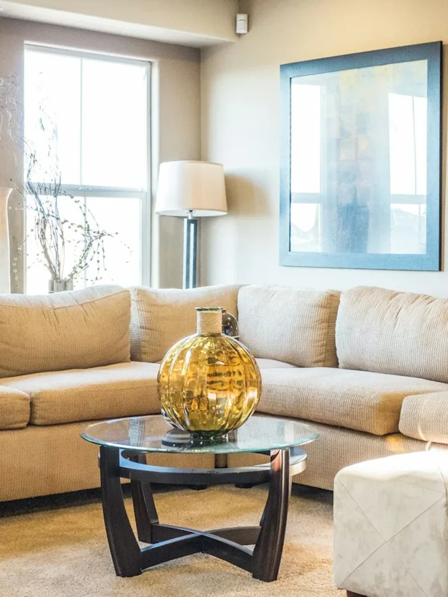 A beige L-shaped sectional sofa around a glass coffee table in a bright room