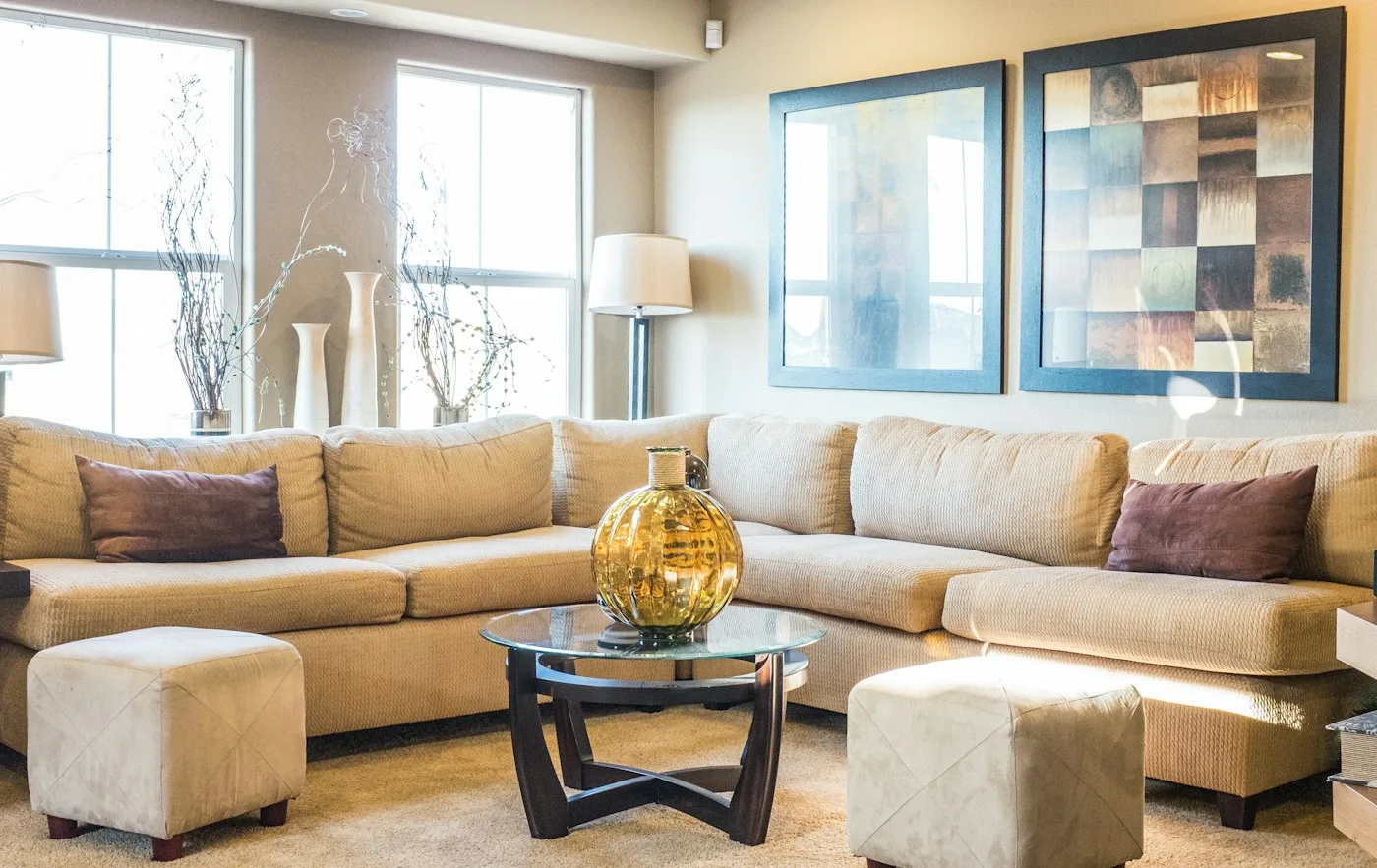 A beige L-shaped sectional sofa around a glass coffee table in a bright room