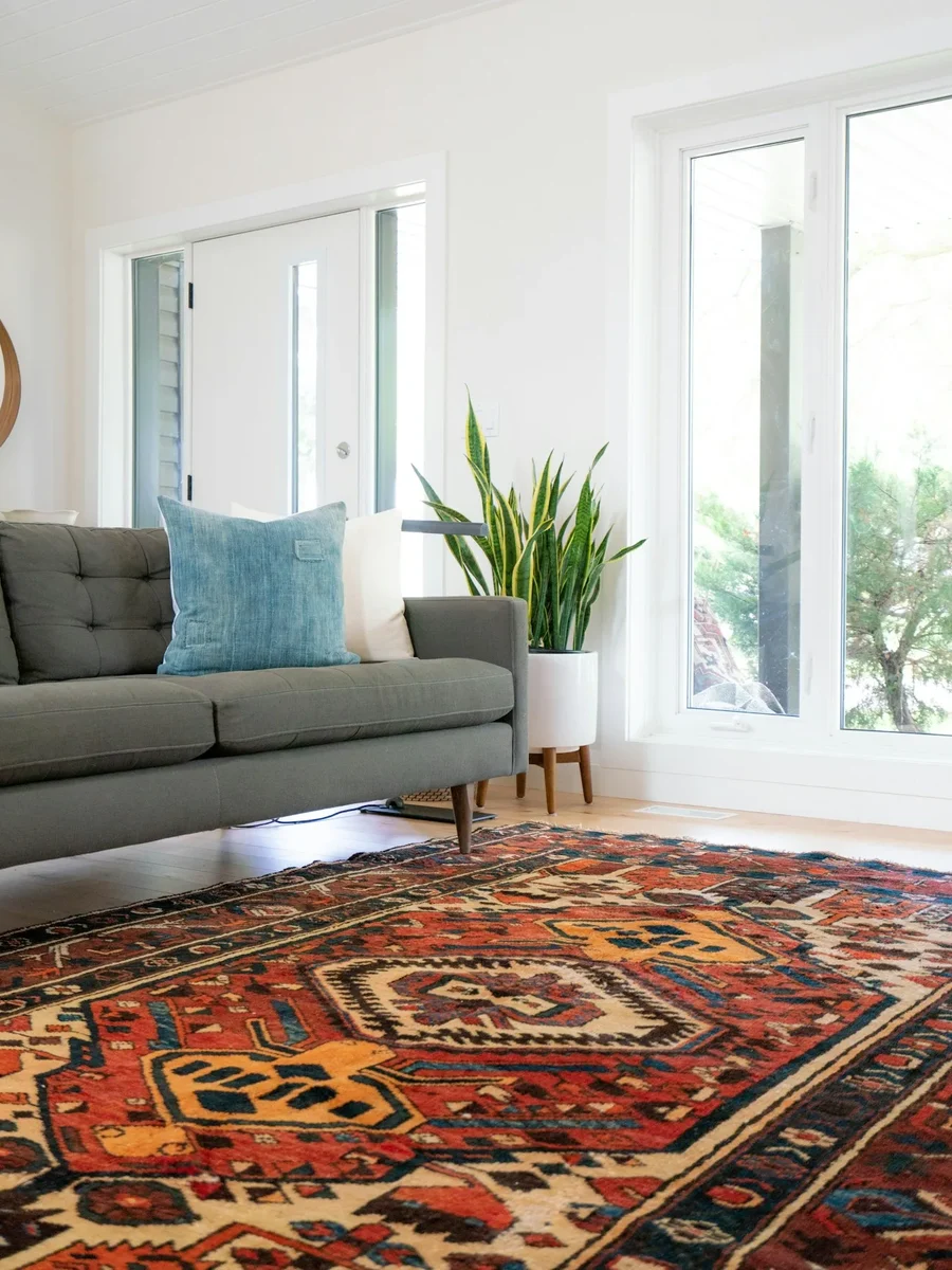 A red hand-knotted rug in a bright living room with a grey sofa