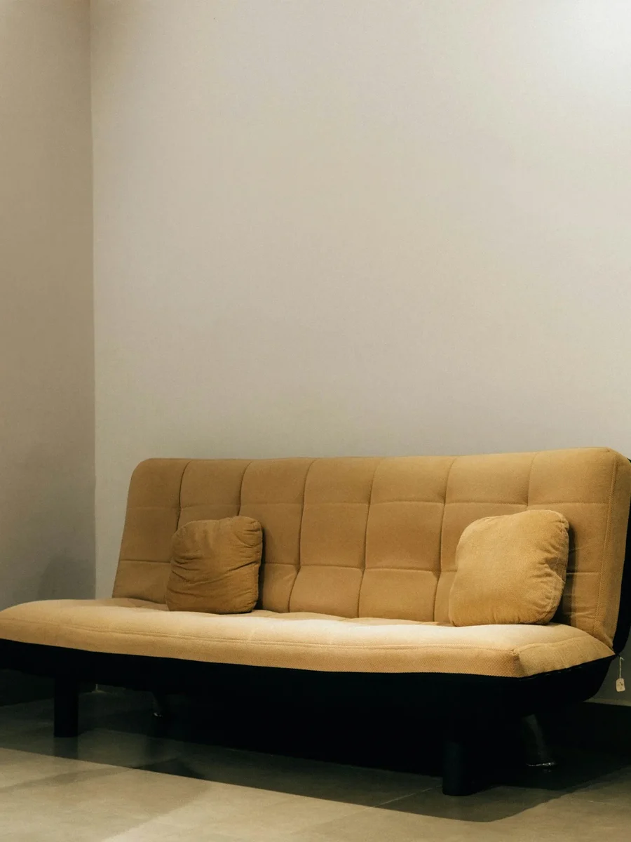 A tan fabric sofa cum bed against a plain wall