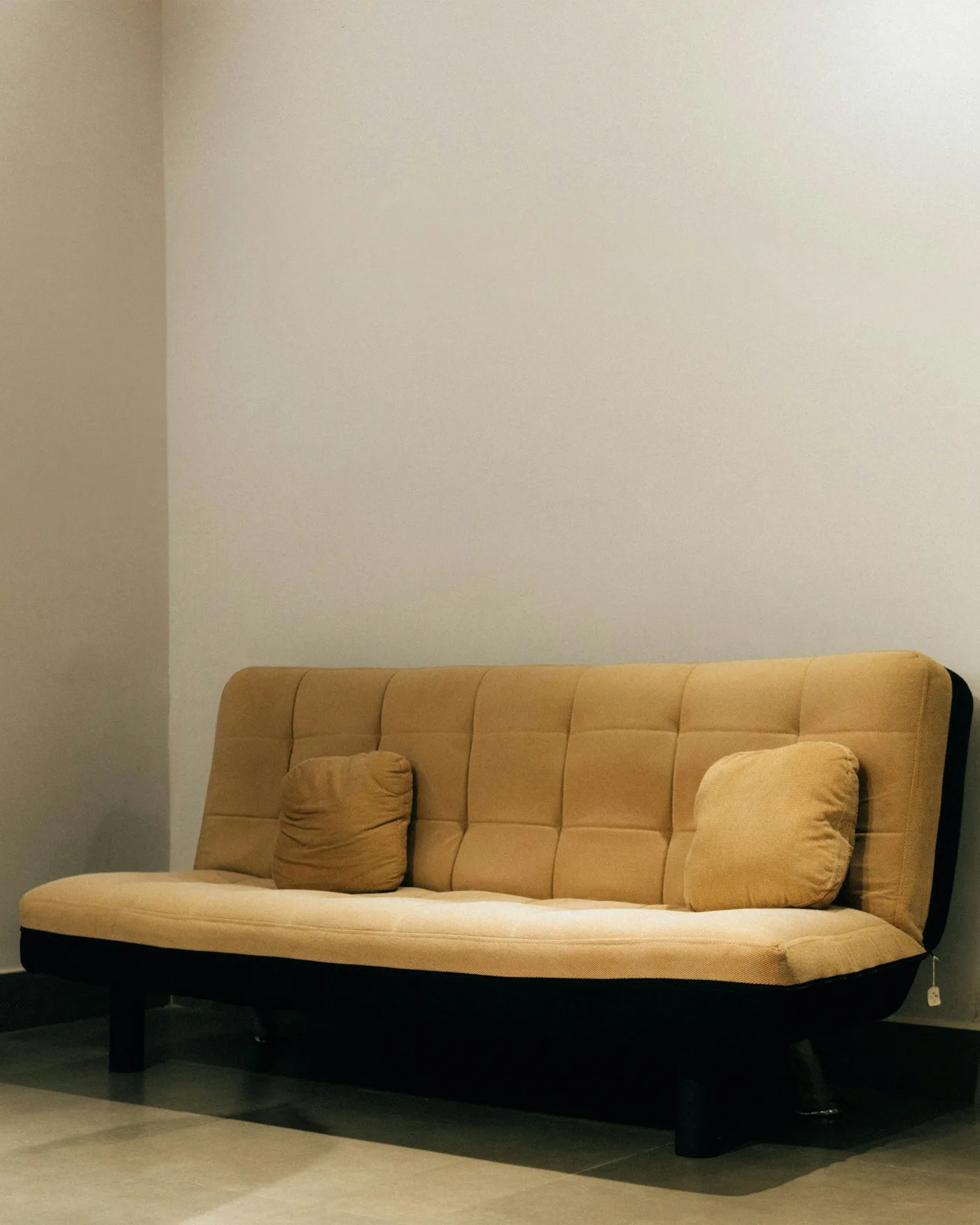 A tan fabric sofa cum bed against a plain wall