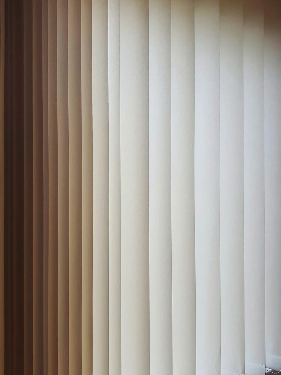 Vertical blind vanes filtering warm light across tall glazing