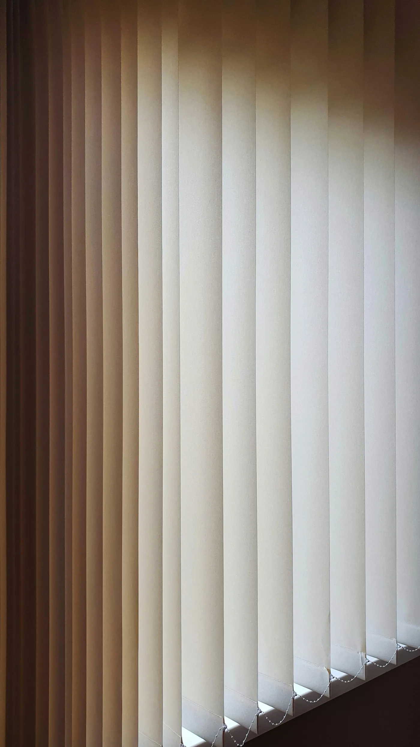 Vertical blind vanes filtering warm light across tall glazing