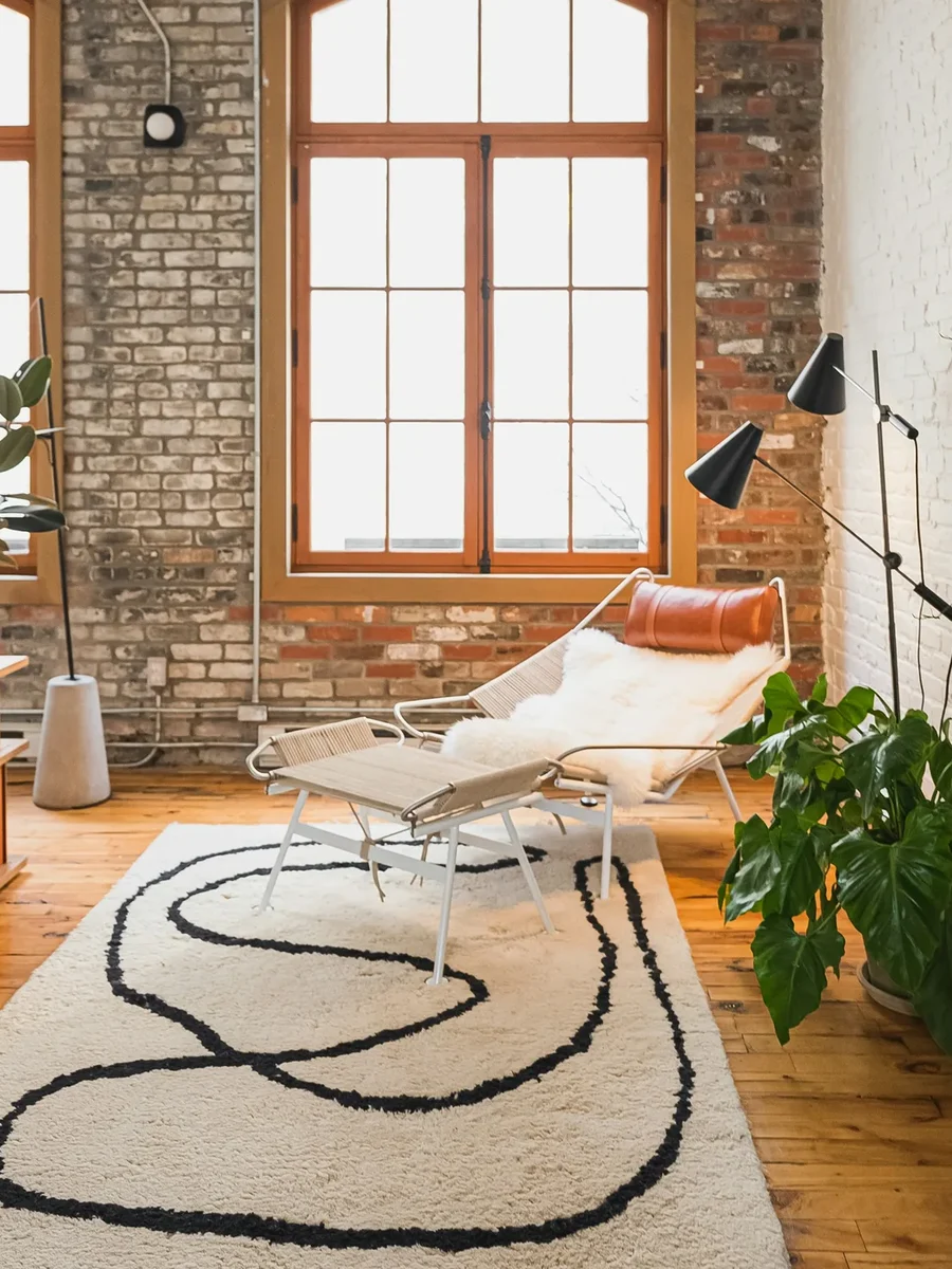 A cream wool rug with a flowing black line, under tall arched windows in a bright living room