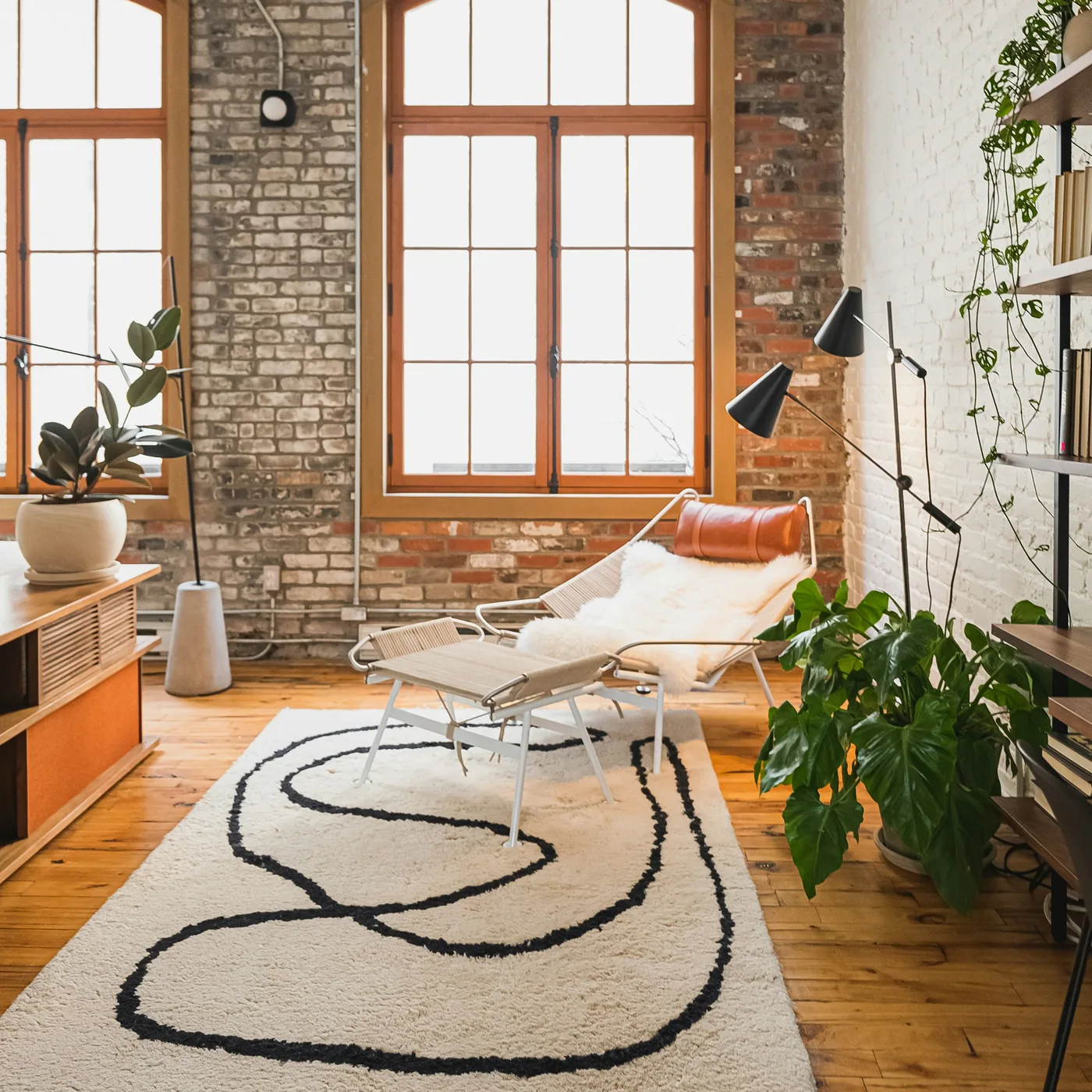 A cream wool rug with a flowing black line, under tall arched windows in a bright living room