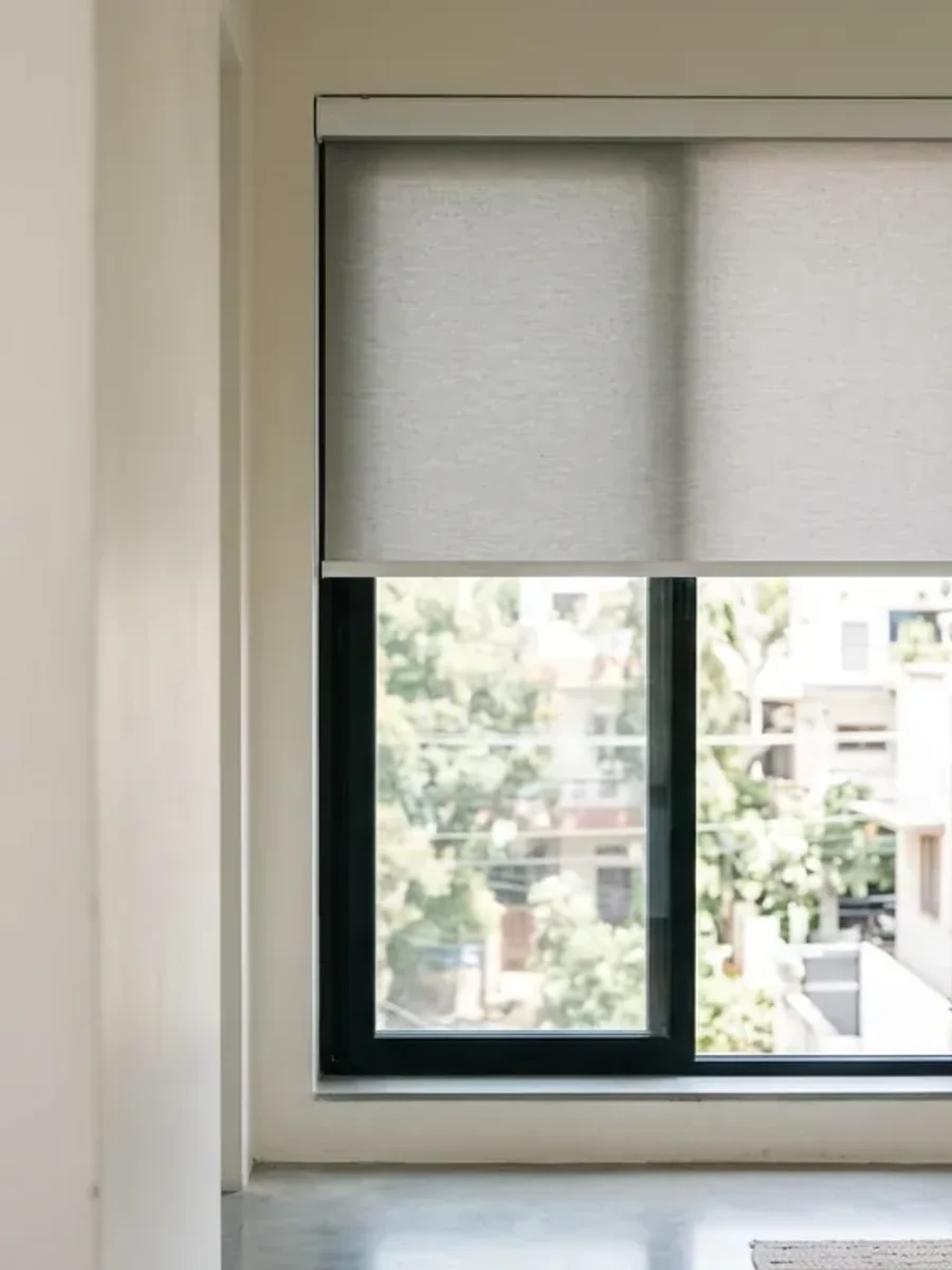 A motorised roller blind part-lowered over a window in a pale interior