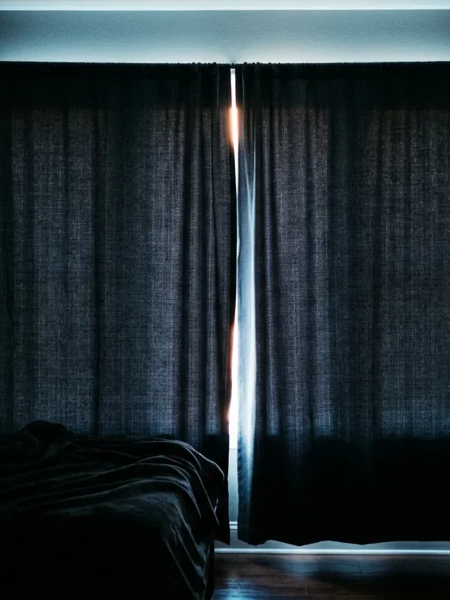 A bedroom darkened by lined blackout curtains with a thin line of daylight at the edge