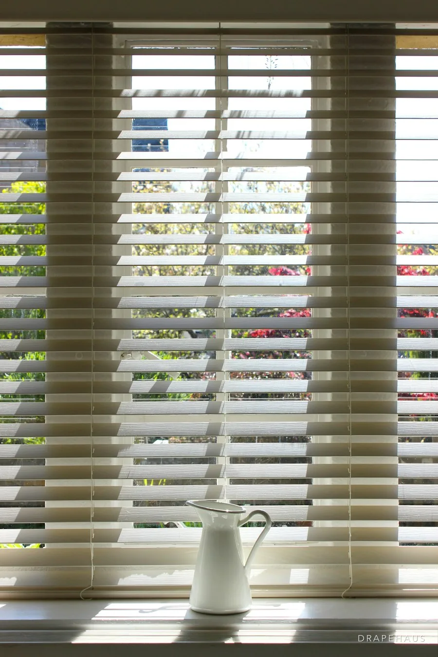 White faux-wood Venetian blinds on a bright window