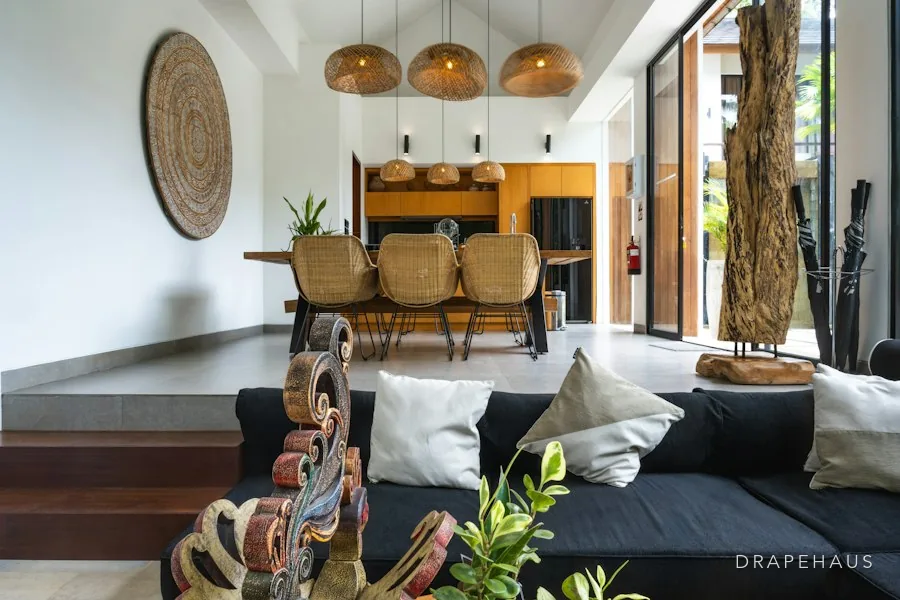 A high-ceilinged villa living and dining room with woven pendant lights and rattan chairs