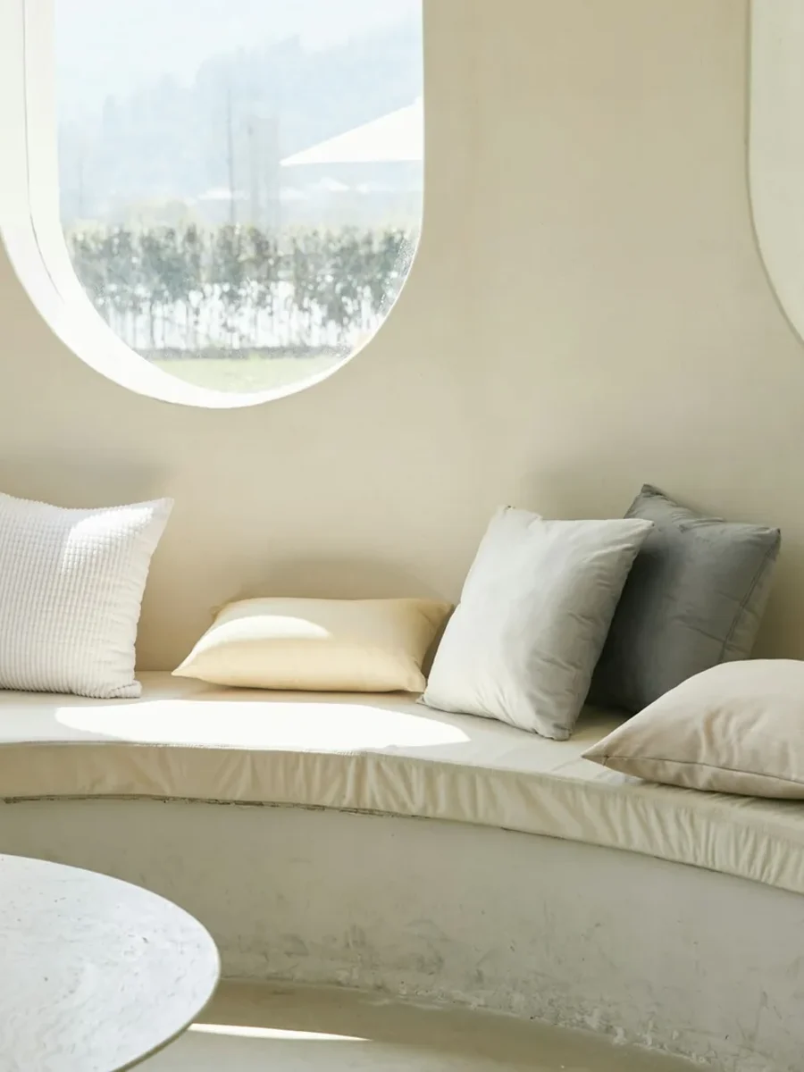 All-white curved built-in seat with pale cushions beneath two oval windows