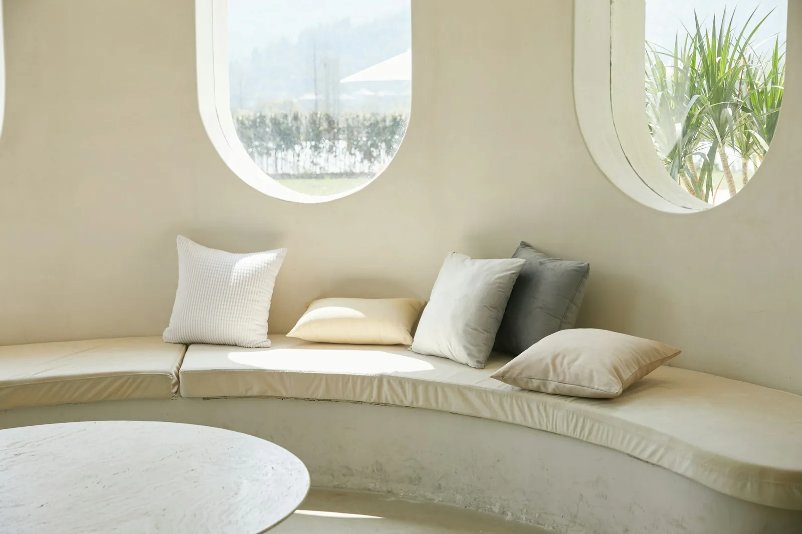 All-white curved built-in seat with pale cushions beneath two oval windows