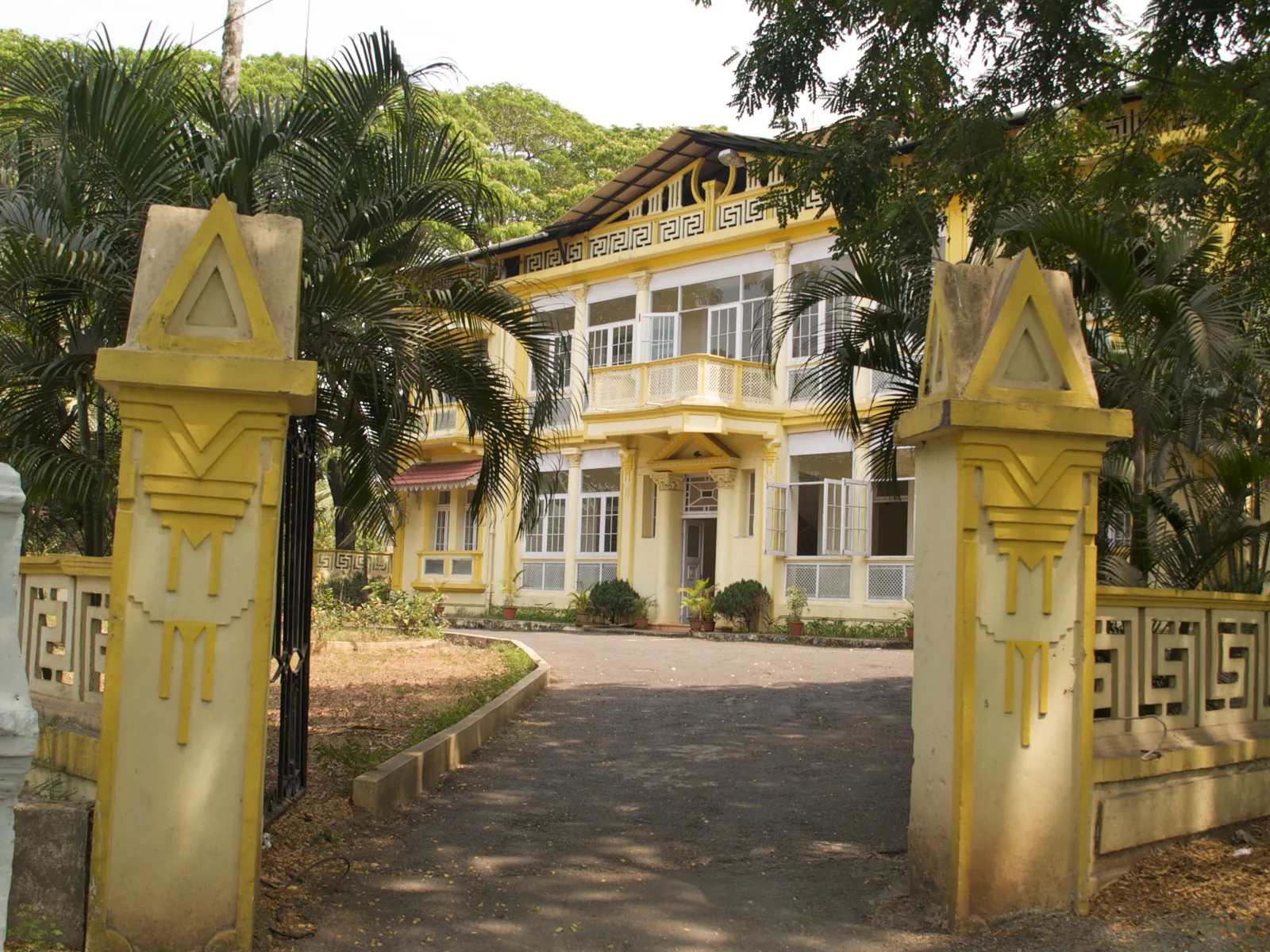 A yellow Art Deco mansion in Panaji seen through stepped geometric gateposts along a curving driveway