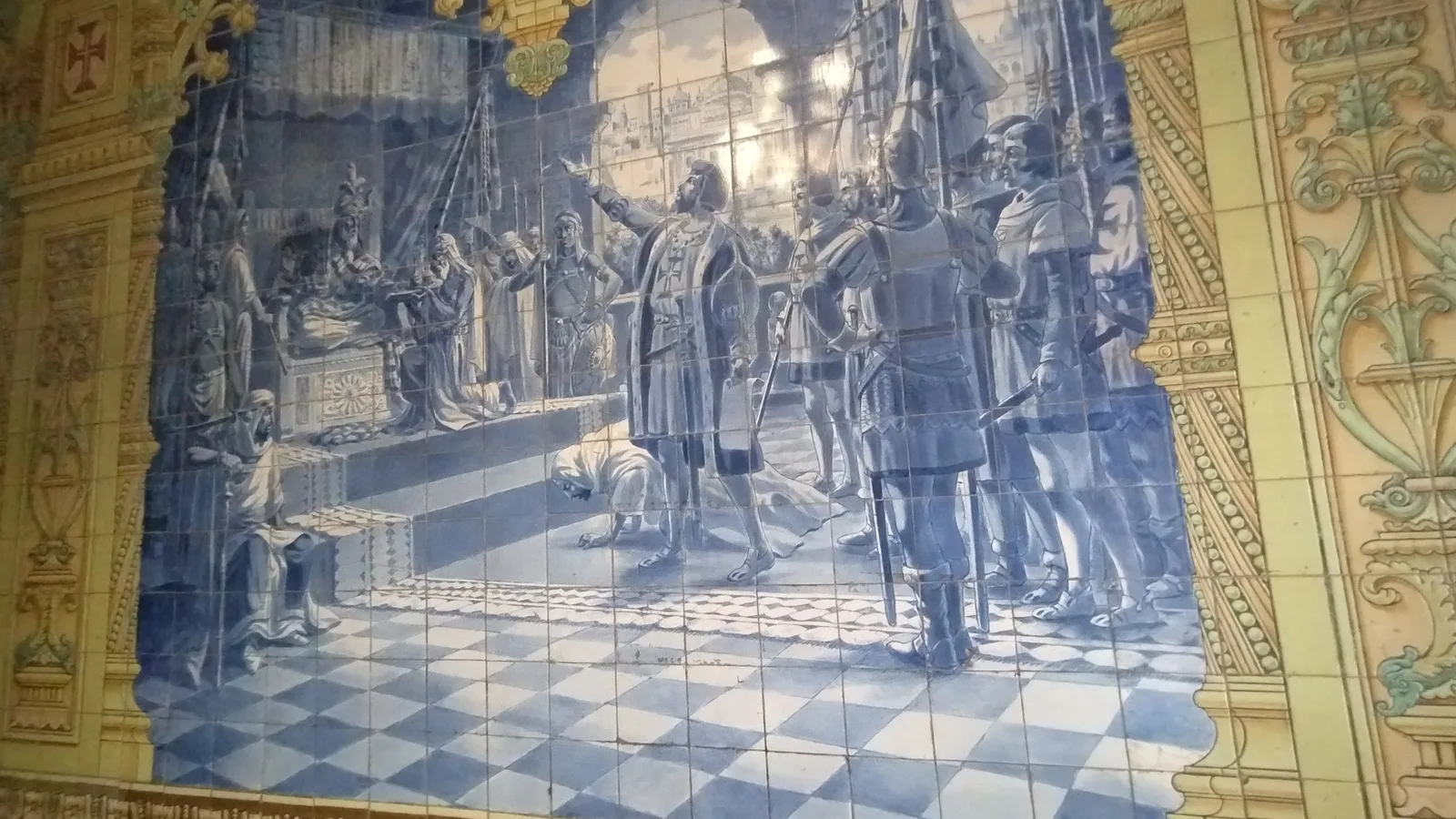 A pre-1961 blue-and-white azulejo panel in Goa framed by yellow patterned tiles, showing a historical court scene