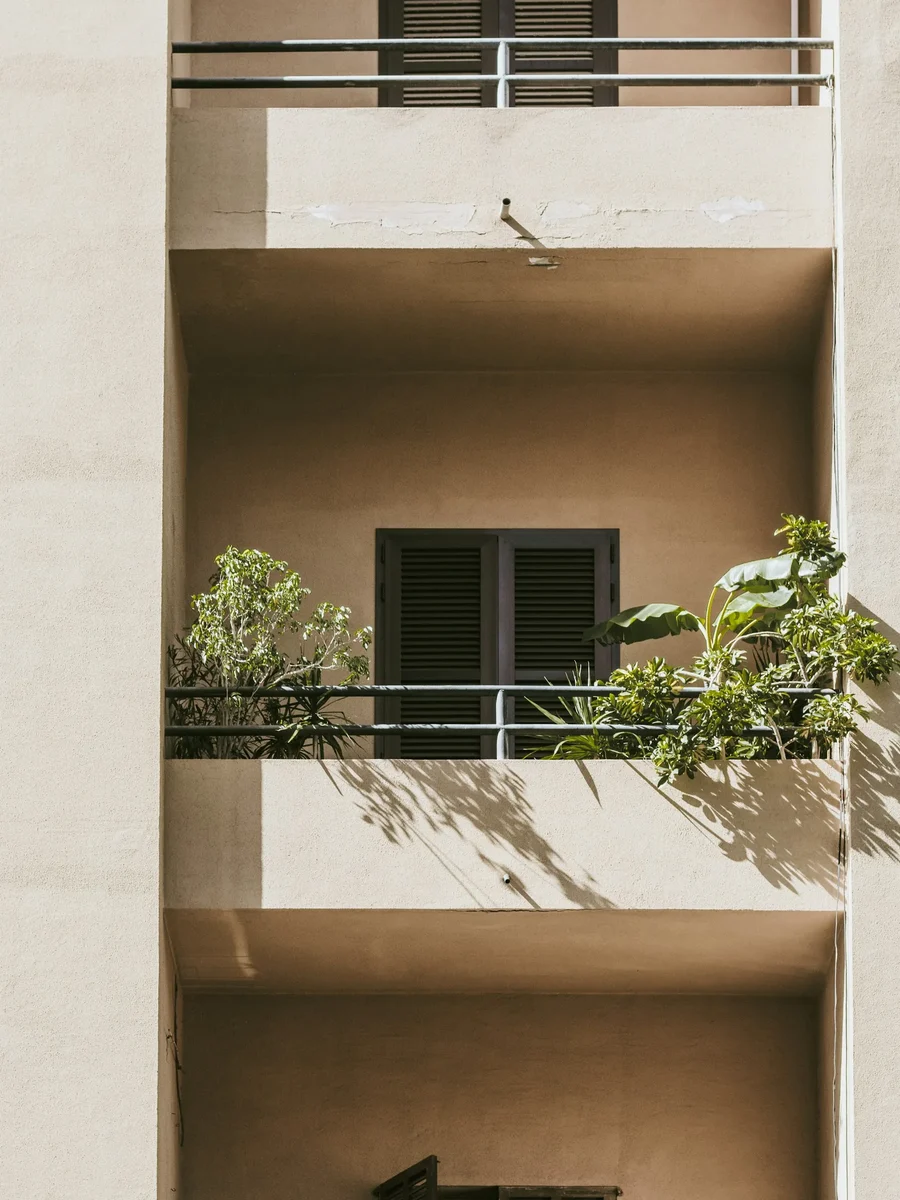 Stacked apartment balconies in warm beige render with dark louvred shutters and potted plants