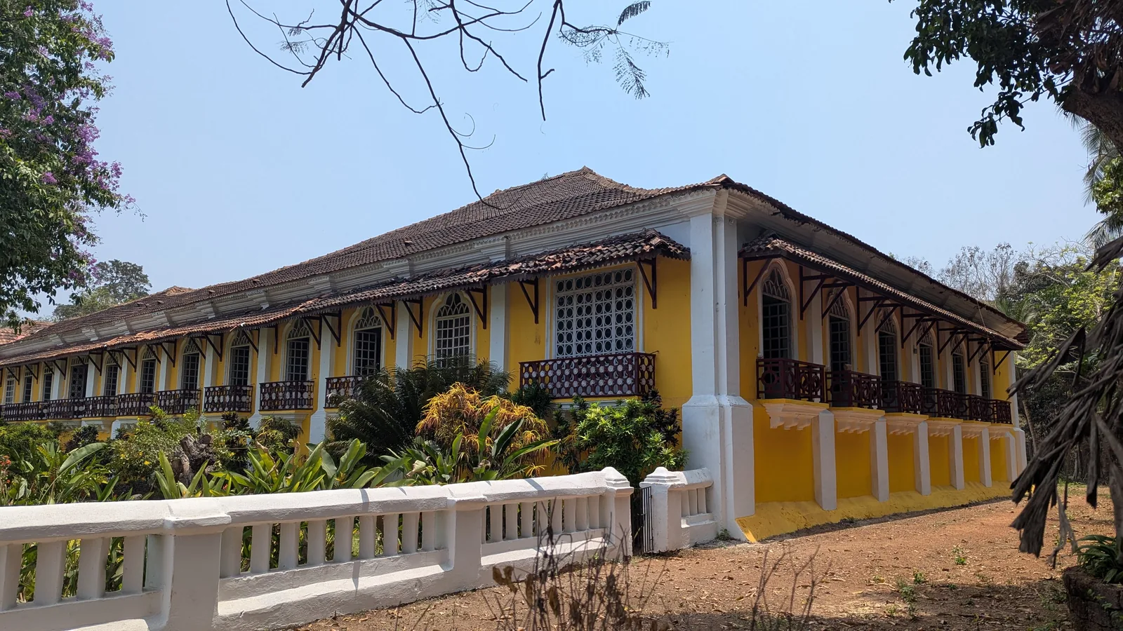 Long yellow facade of the Menezes Braganza House in Chandor, Salcete, with tiled roof and wooden balconies