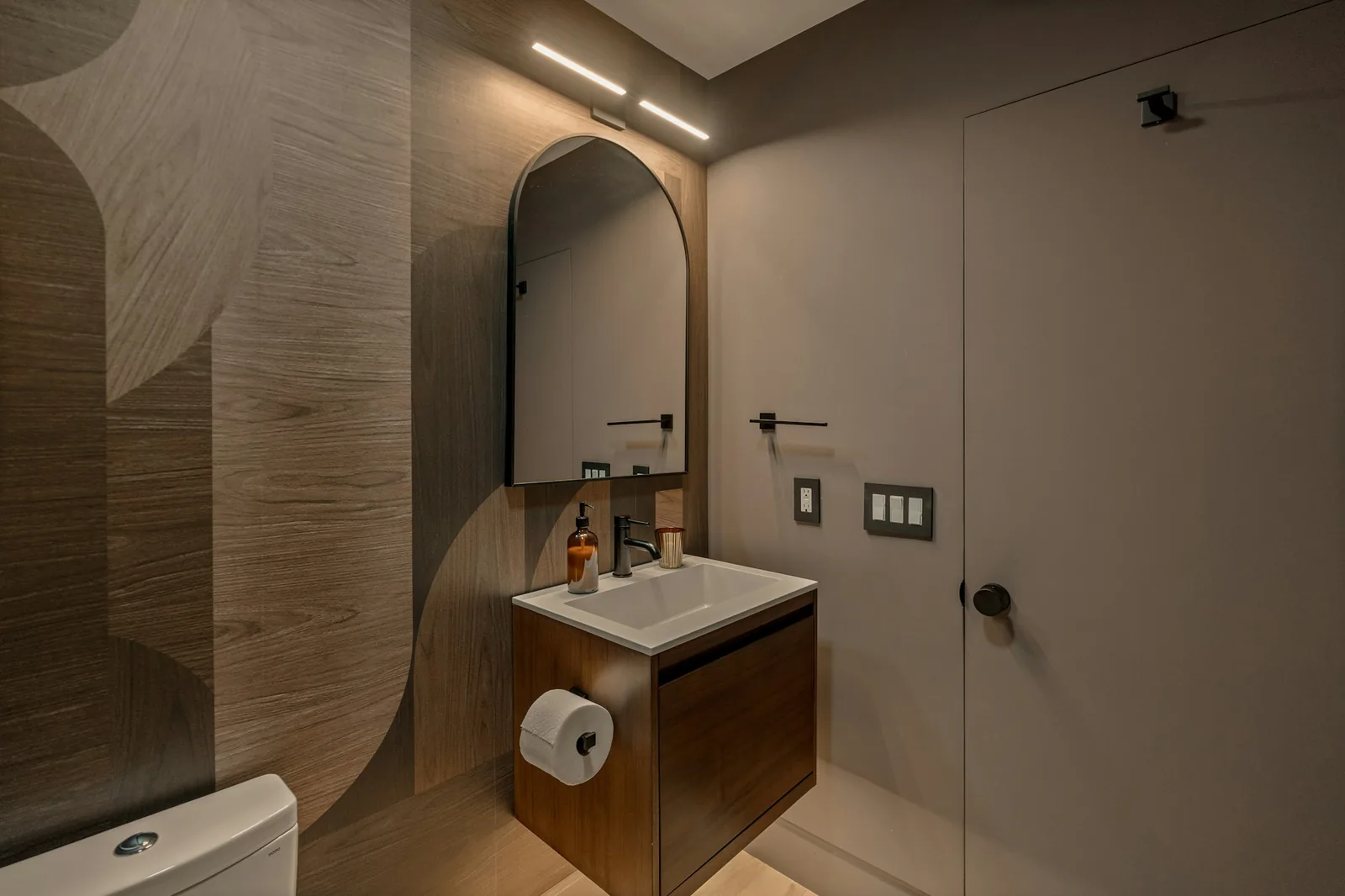 Small powder room with a large-scale wood-grain wallpaper, arched mirror and wall-hung vanity