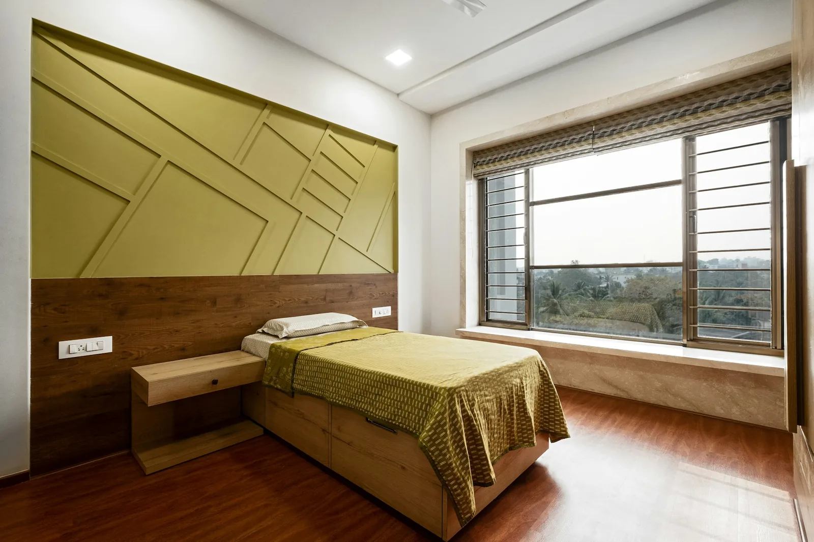 Bedroom headboard wall with olive geometric panelling above a wood-laminate wainscot