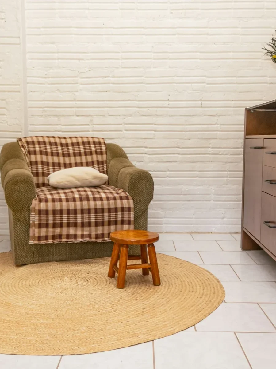 Round natural jute rug on white tiles under an armchair and small wooden stool