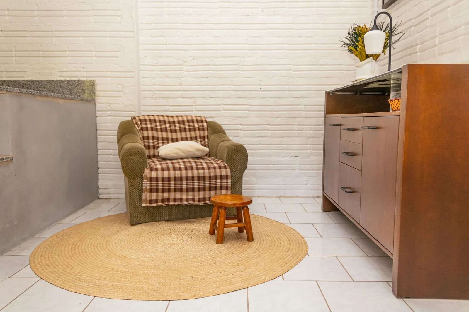 Round natural jute rug on white tiles under an armchair and small wooden stool