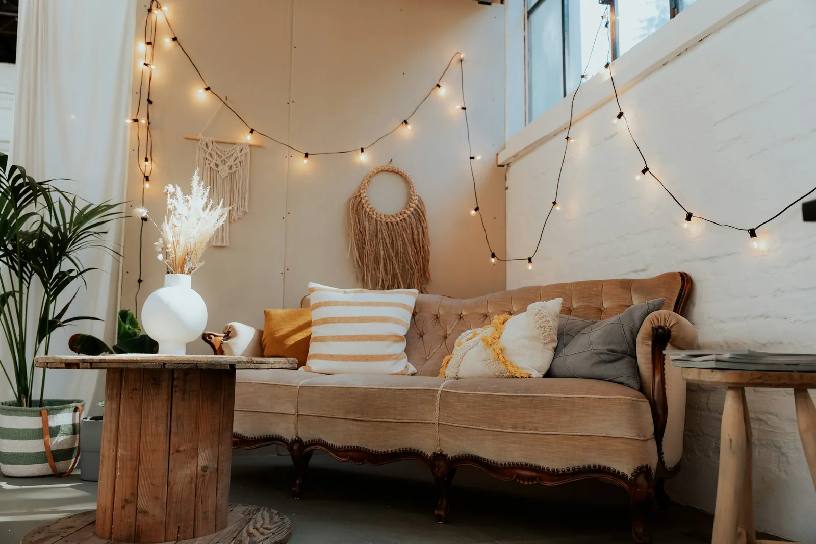 Boho corner with a vintage tufted sofa, macramé and woven wall hangings, string lights and a cable-reel table