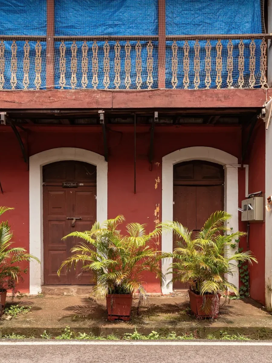 A weathered red Portuguese-era house in Fontainhas, its upper balcony wrapped in blue tarpaulin