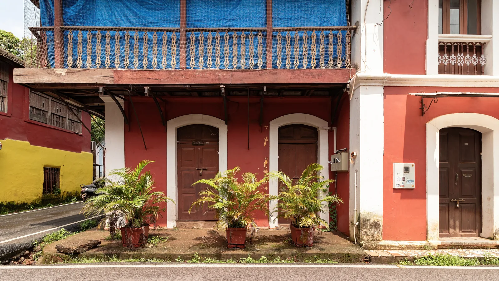A weathered red Portuguese-era house in Fontainhas, its upper balcony wrapped in blue tarpaulin