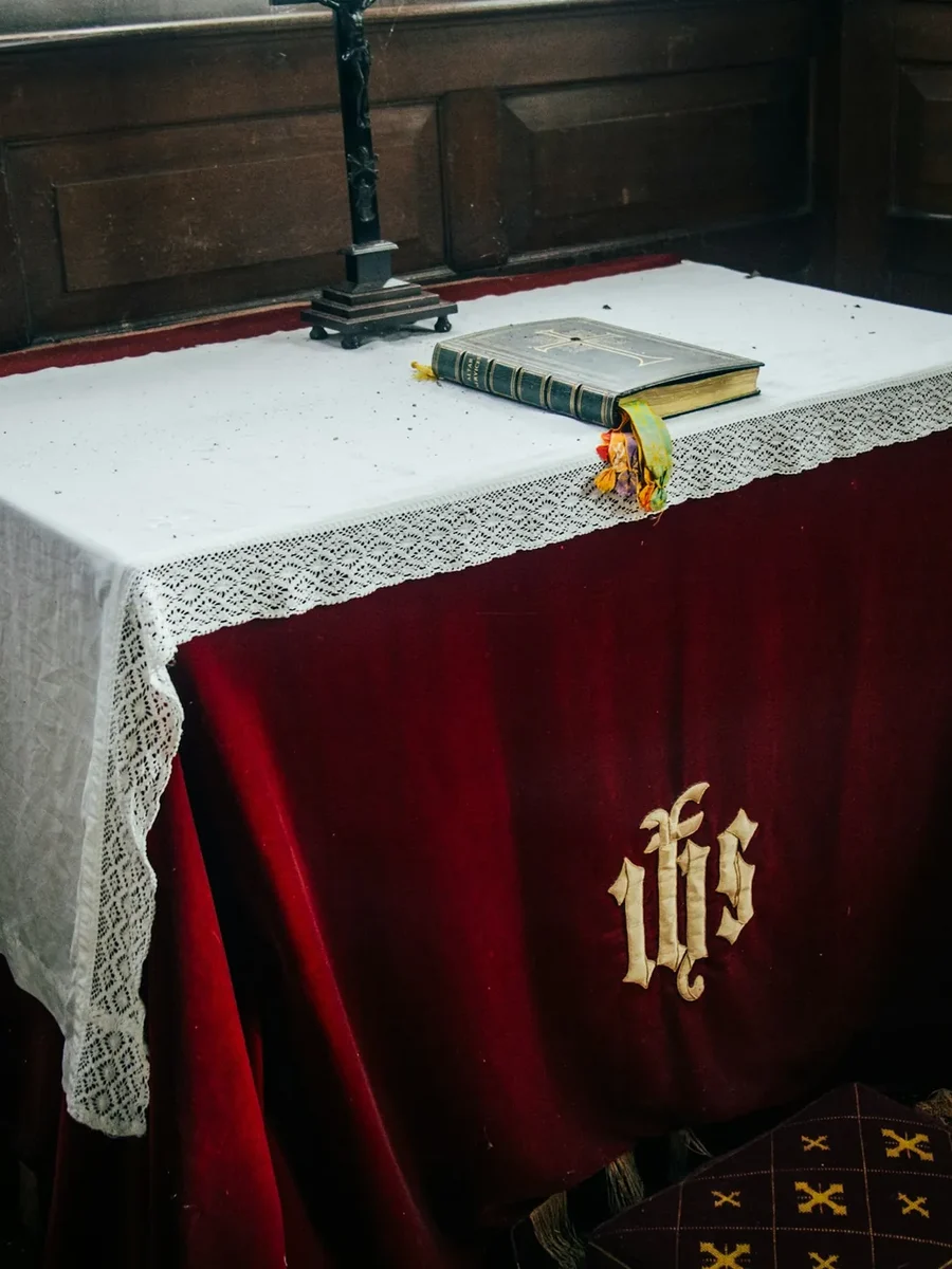 Chapel altar dressed in a red velvet frontal with an embroidered IHS monogram and white lace cloth