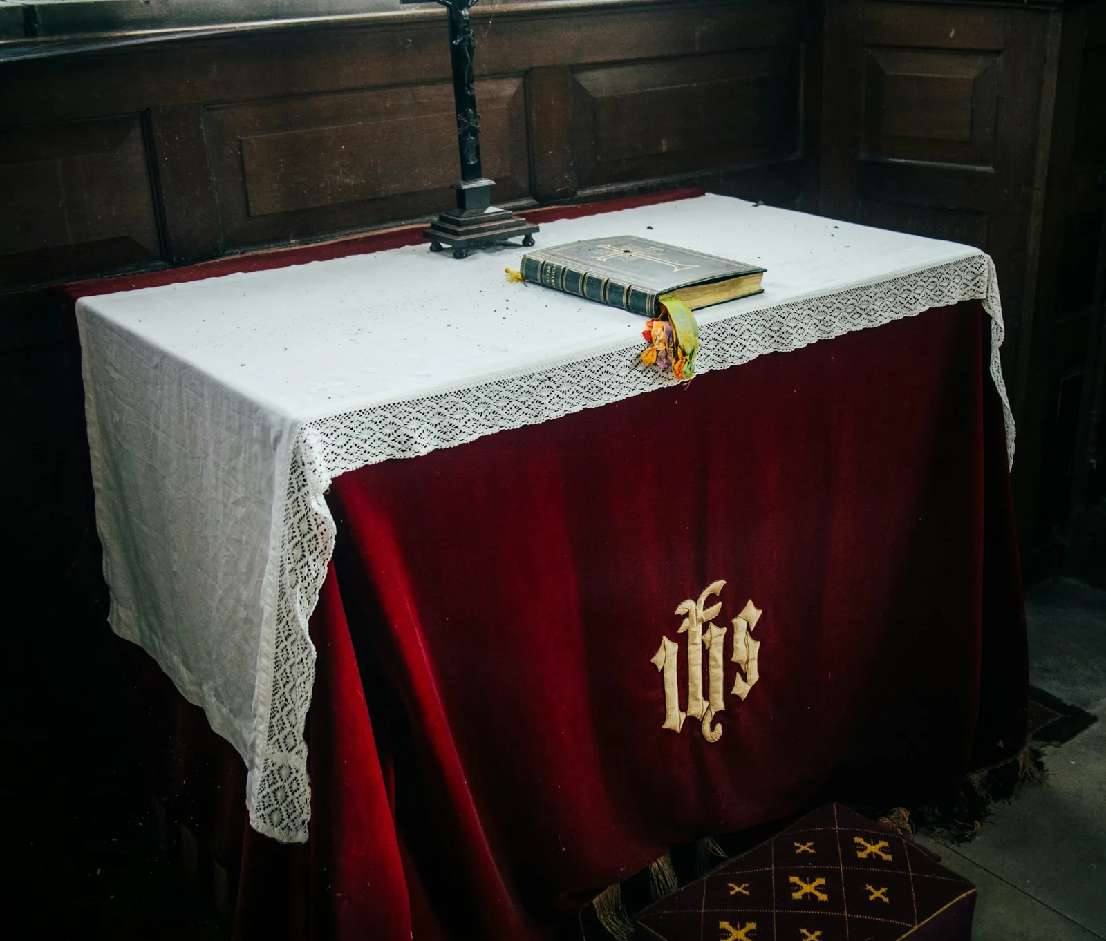 Chapel altar dressed in a red velvet frontal with an embroidered IHS monogram and white lace cloth