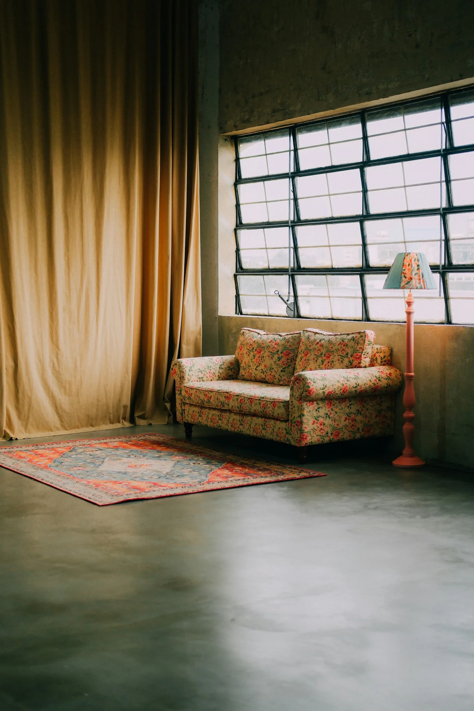 Mustard-gold floor-length curtains beside a steel-framed window, a floral sofa and a red rug