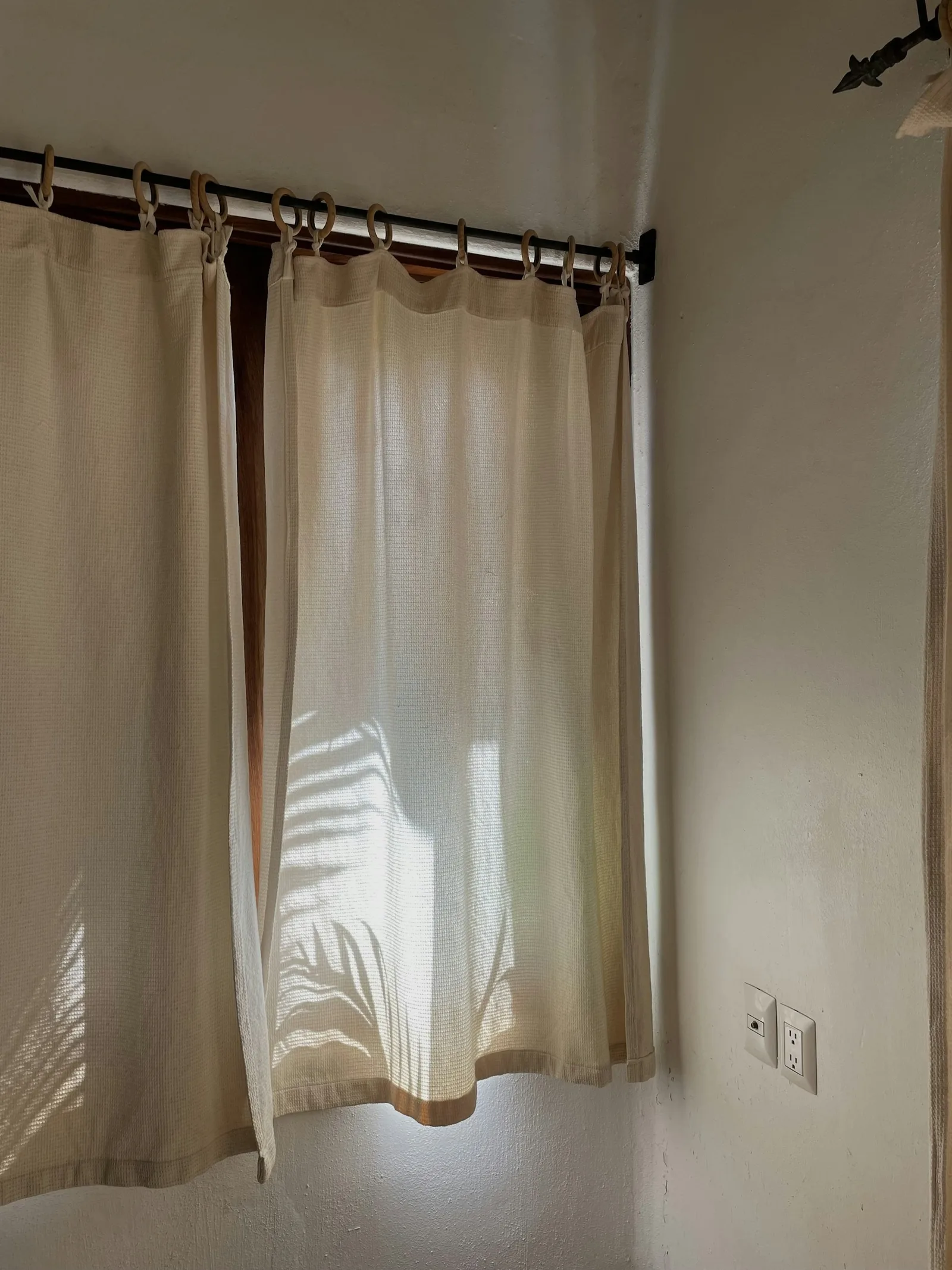 Cream cotton curtains clipped to rings on a slim black rod across a corner window