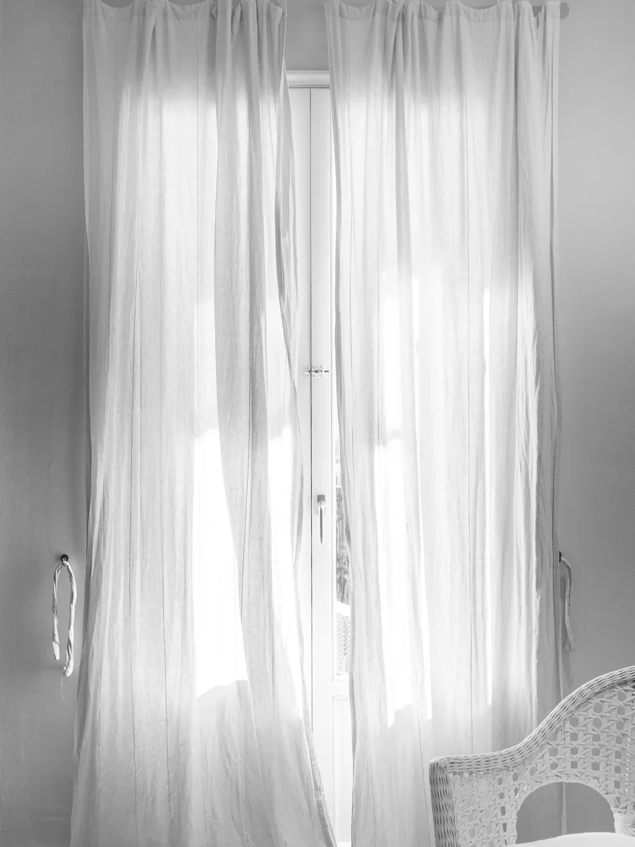 White tab-top sheer curtains hanging from a black steel rod that extends past a tall window