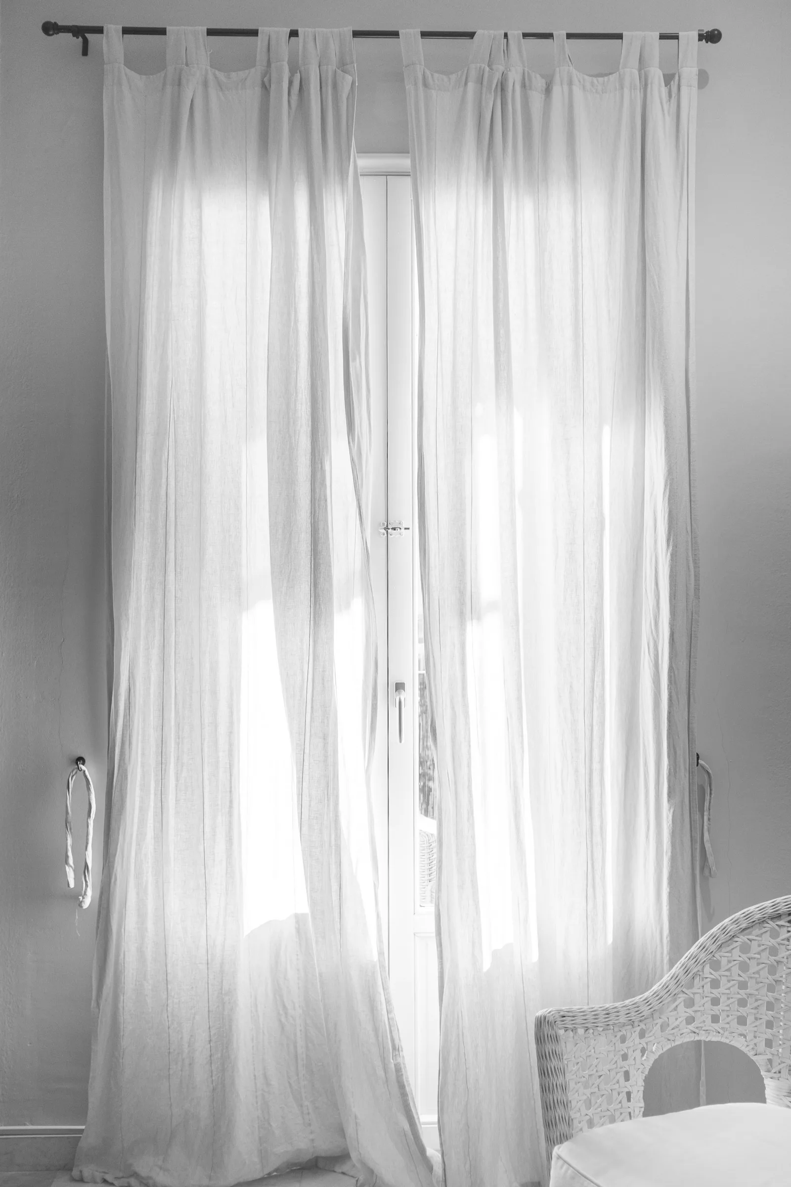White tab-top sheer curtains hanging from a black steel rod that extends past a tall window