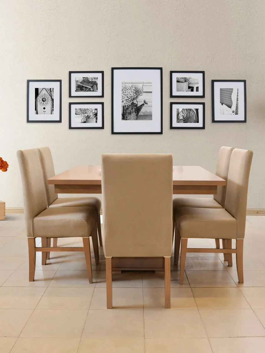 A dining table with upholstered beige chairs below a gallery wall of black-framed photographs on a tiled floor