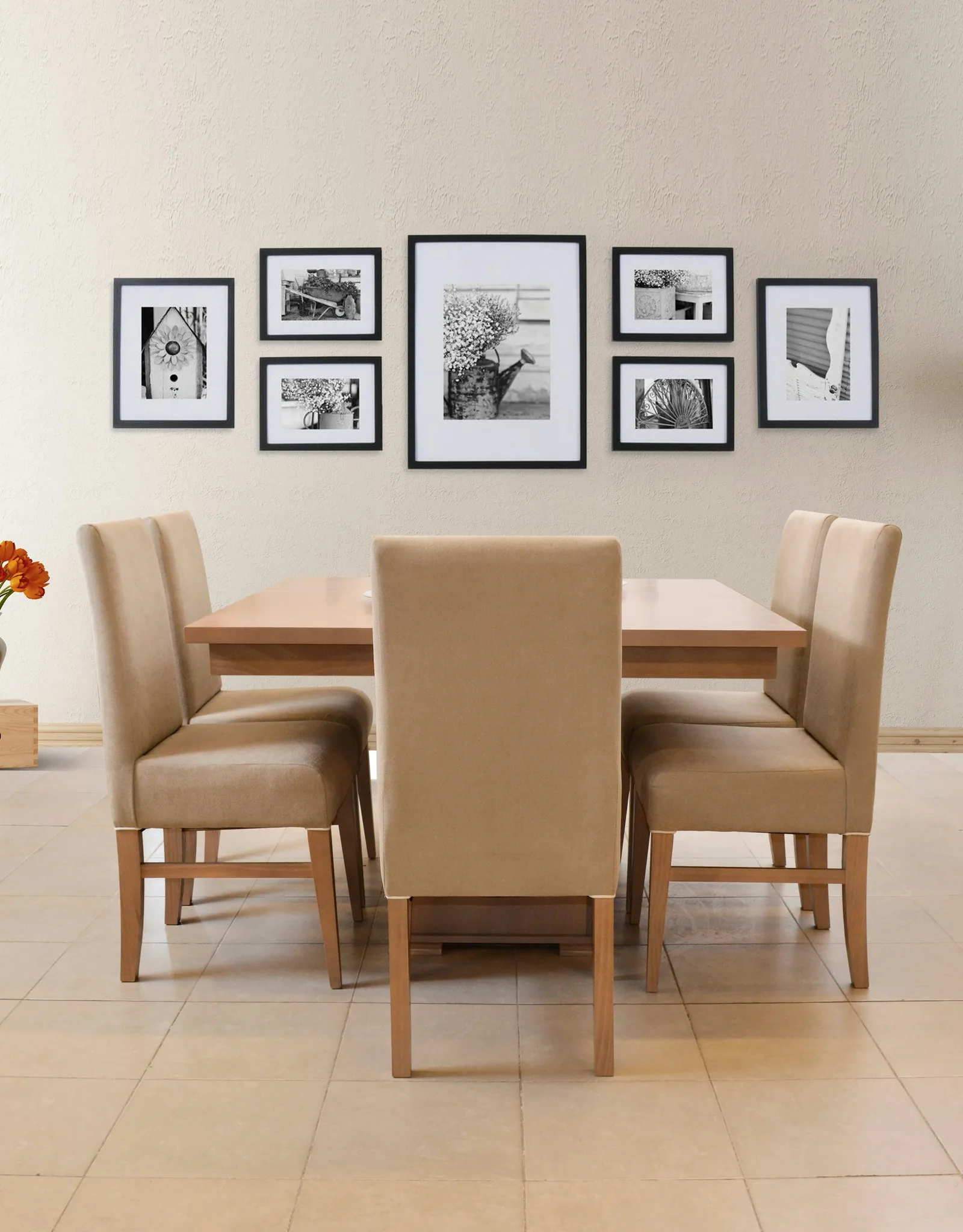 A dining table with upholstered beige chairs below a gallery wall of black-framed photographs on a tiled floor