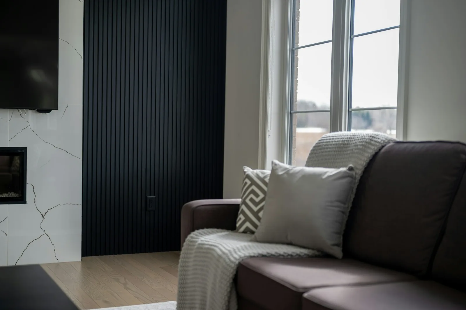 Black vertical fluted panel wall beside a marble fireplace surround and a brown sofa