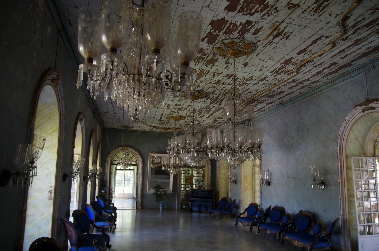 The ballroom of the Menezes Braganza house in Chandor, with crystal chandeliers, arched windows and blue chairs