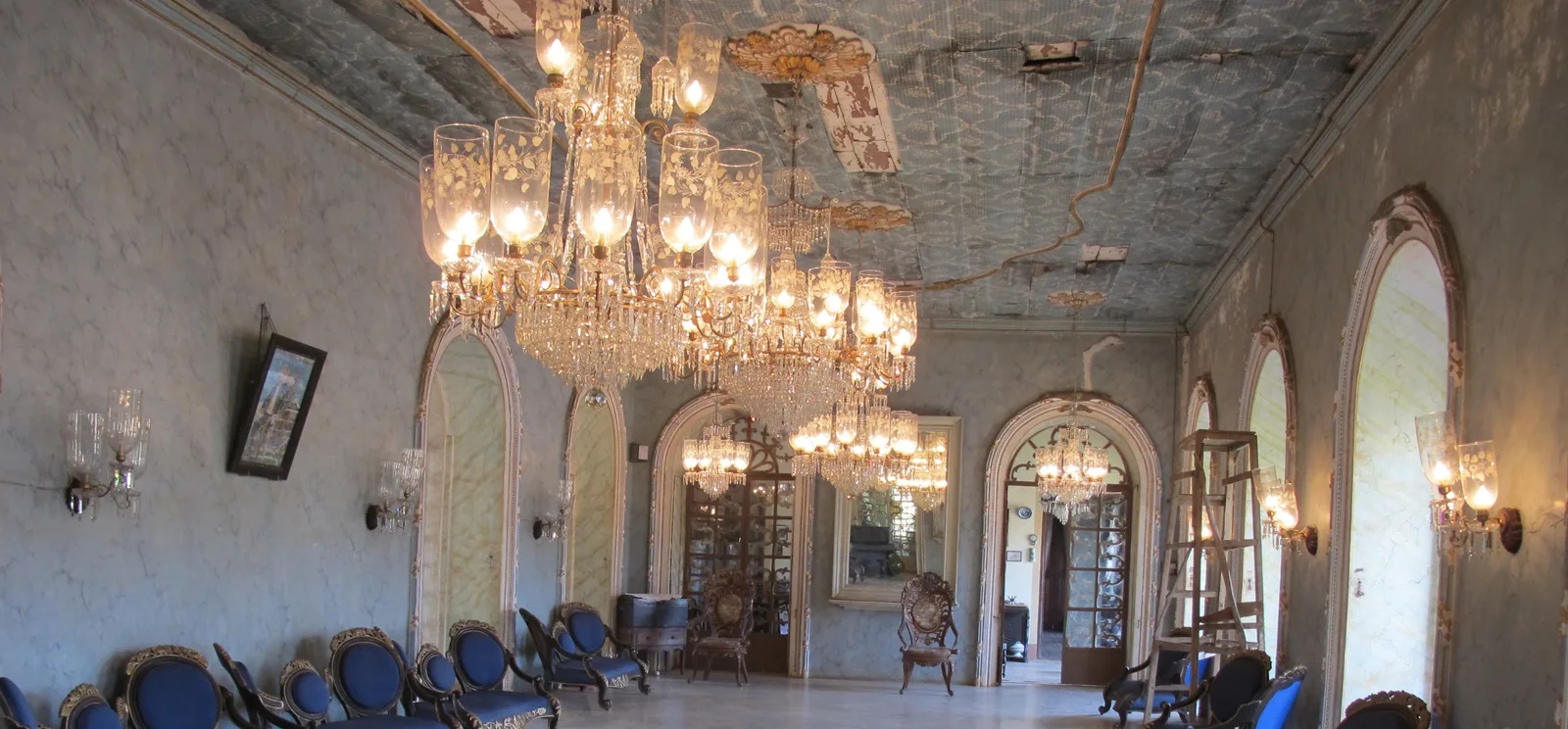 Crystal chandeliers and wall sconces hanging in the long salon of the Braganza mansion in Chandor