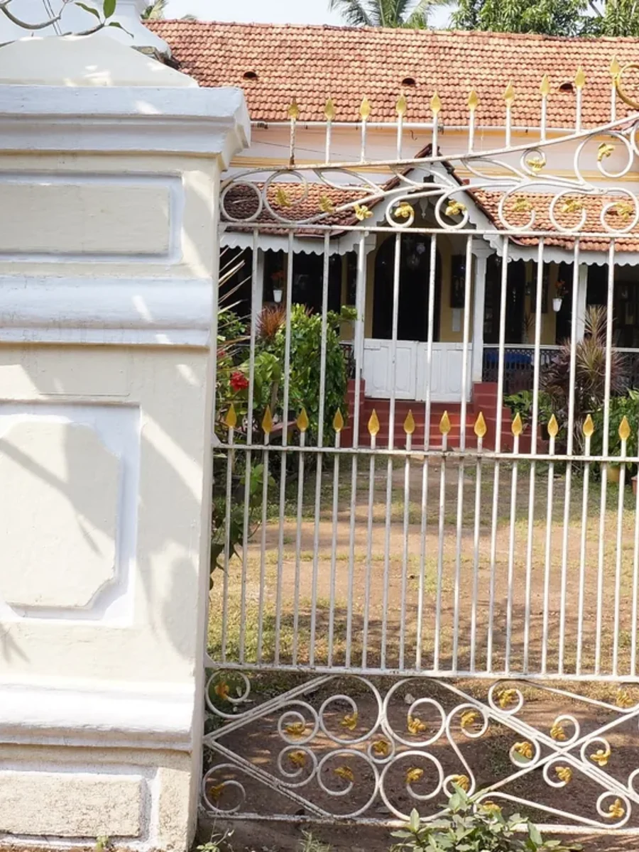 Whitewashed compound wall, square gate pillar and scrolled iron gate in front of a Goan house in Santa Cruz