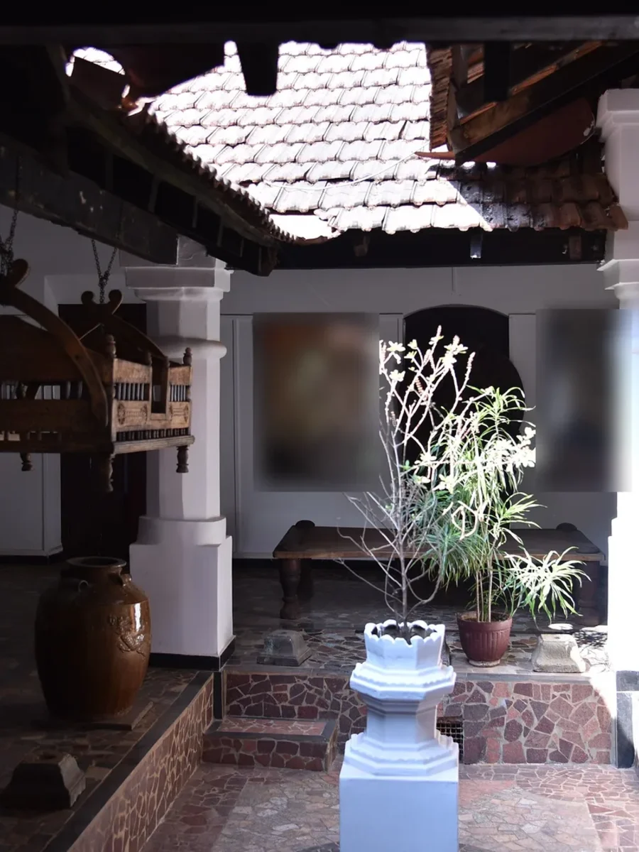 The open inner courtyard of a historic Panjim house with white pillars, a tiled roof and a tulsi stand