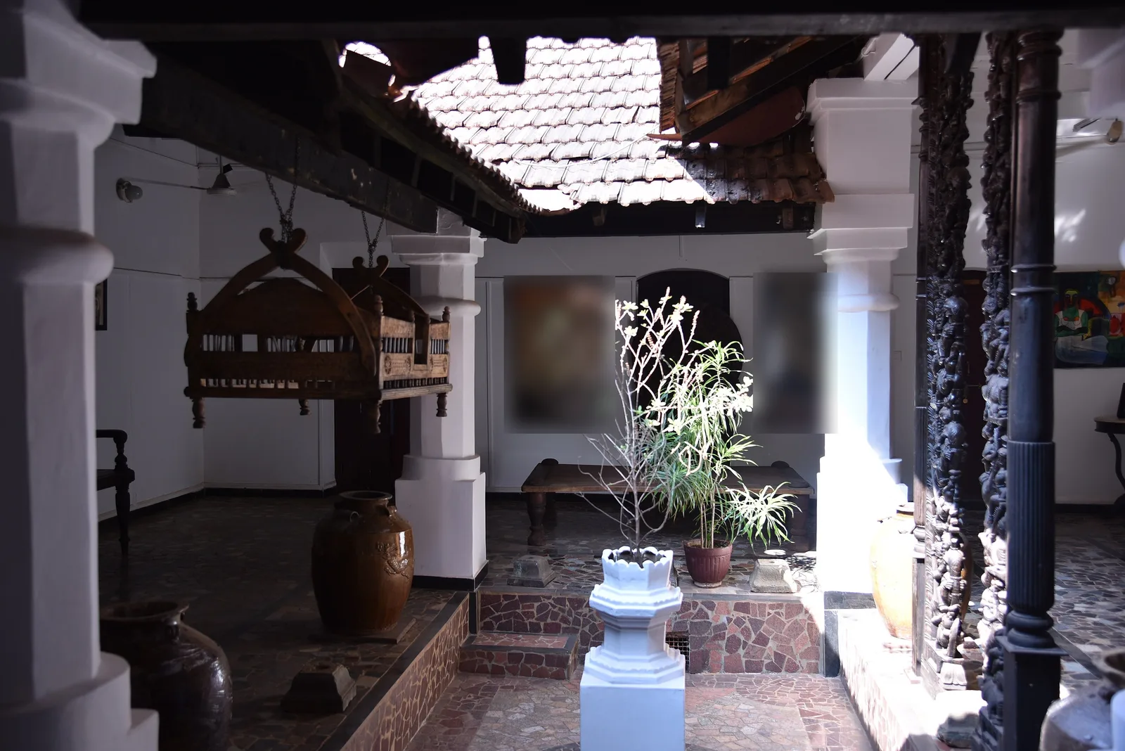 The open inner courtyard of a historic Panjim house with white pillars, a tiled roof and a tulsi stand