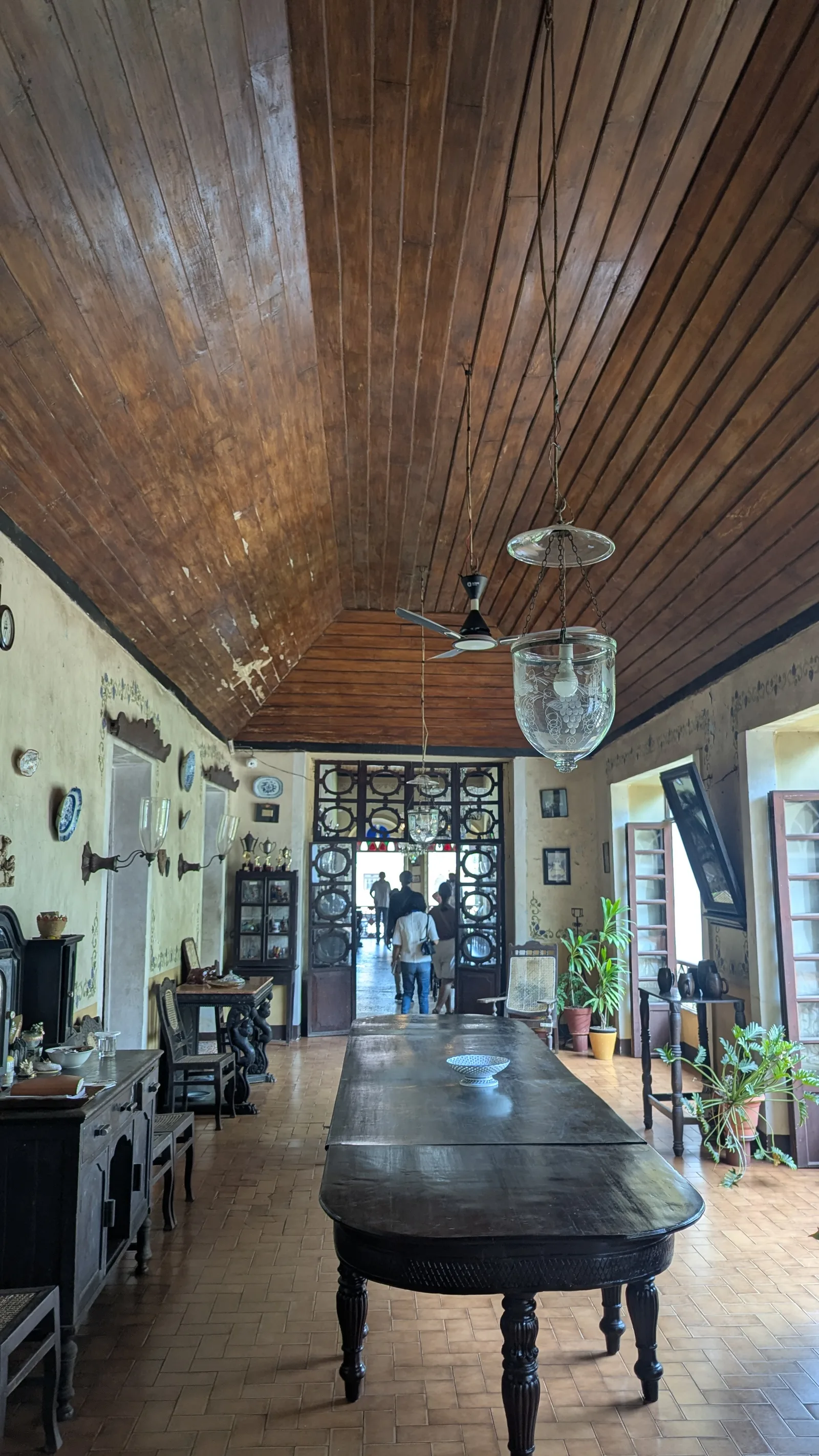 The long dining room of the Menezes Braganza house with an extendable table, timber ceiling and glass lamps