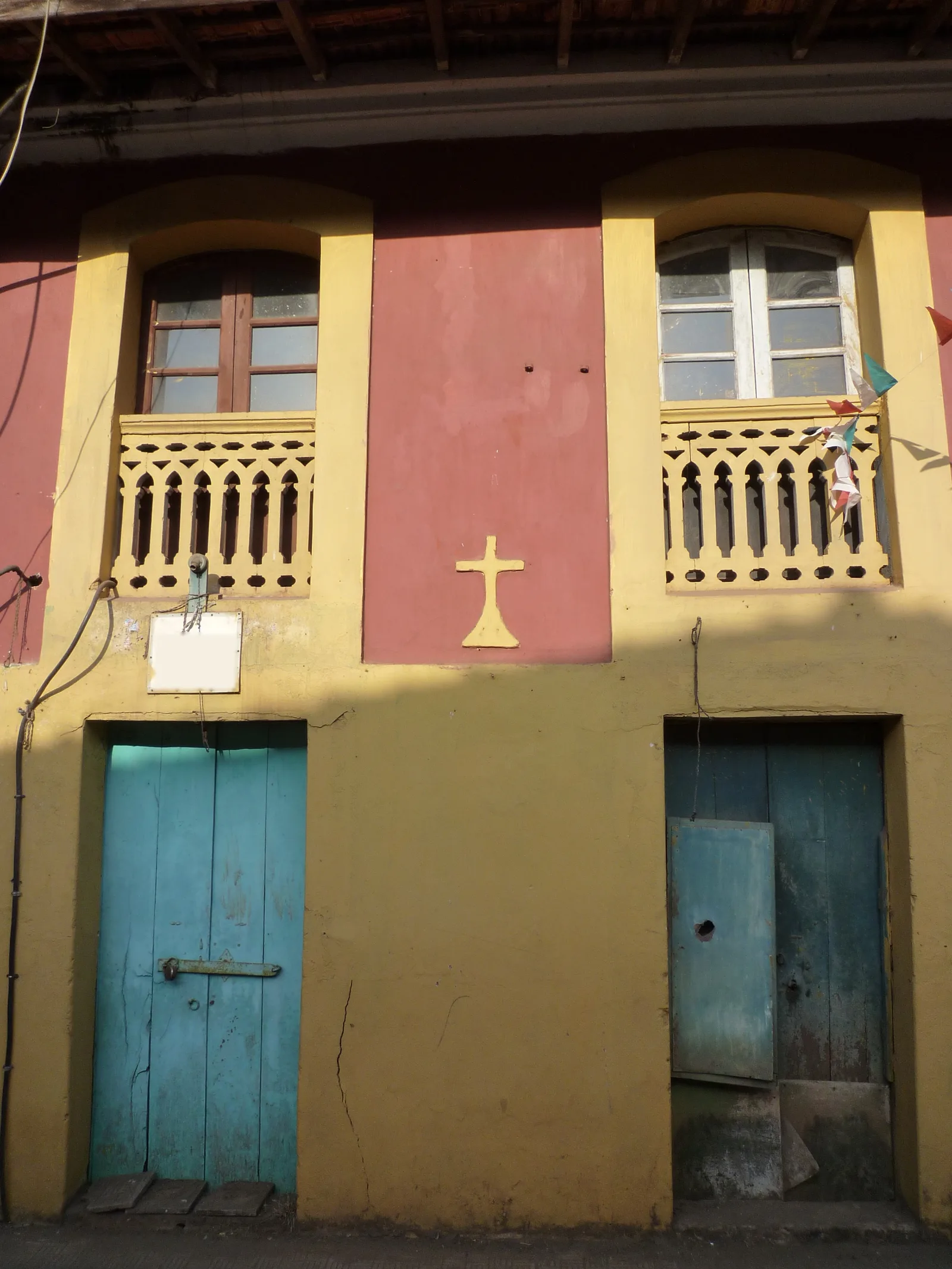 Two weathered turquoise wooden doors in a yellow and red Fontainhas facade beneath balustraded balconies