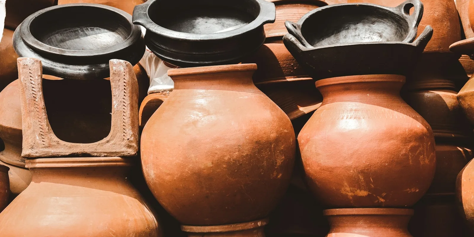 Stacked unglazed terracotta pots and black clay cooking vessels at a pottery stall in India