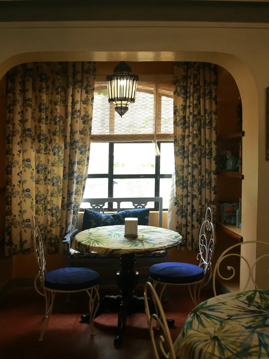 Arched alcove with blue floral curtains, a lantern and iron chairs in a warm Indian interior