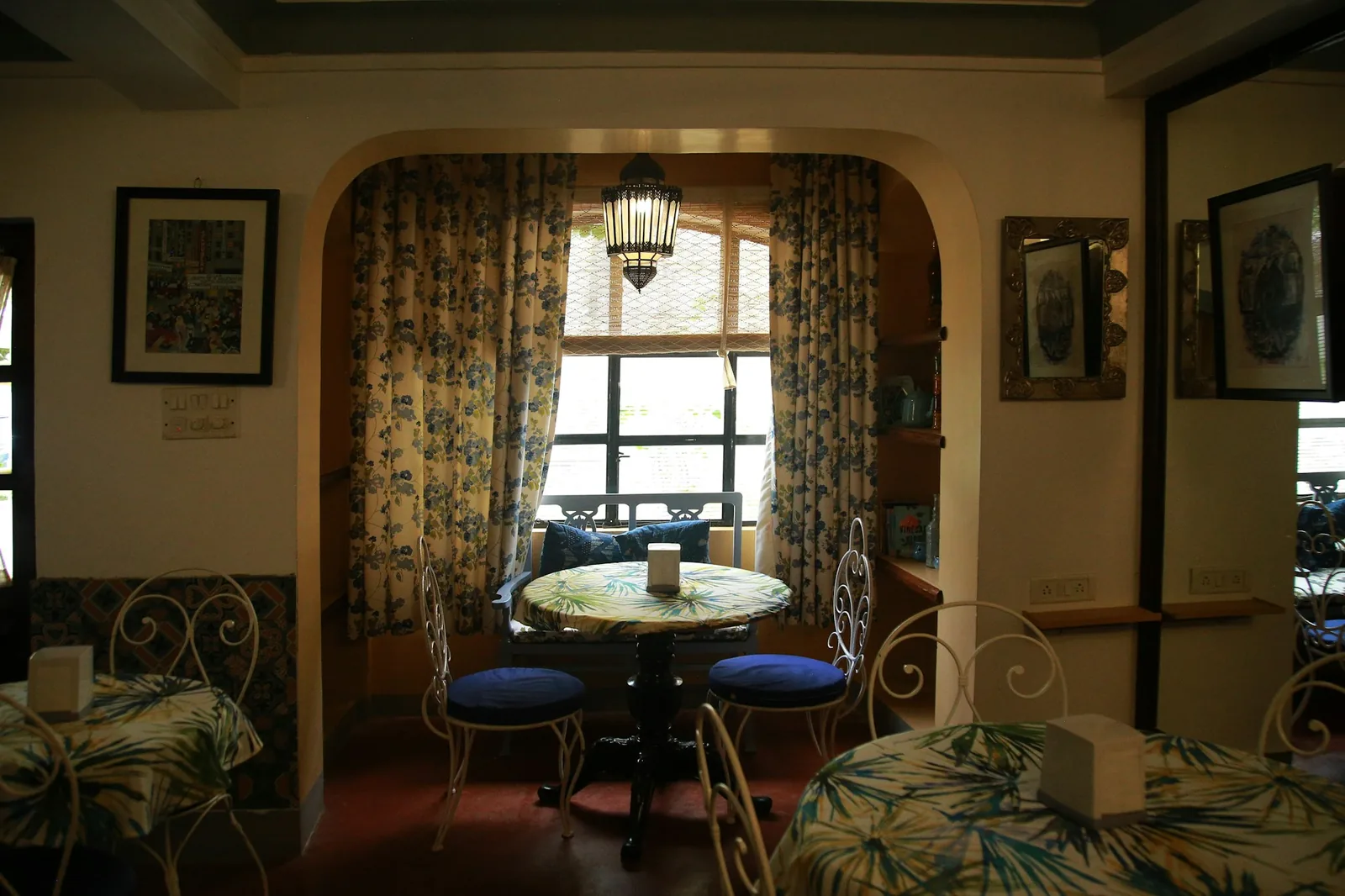 Arched alcove with blue floral curtains, a lantern and iron chairs in a warm Indian interior