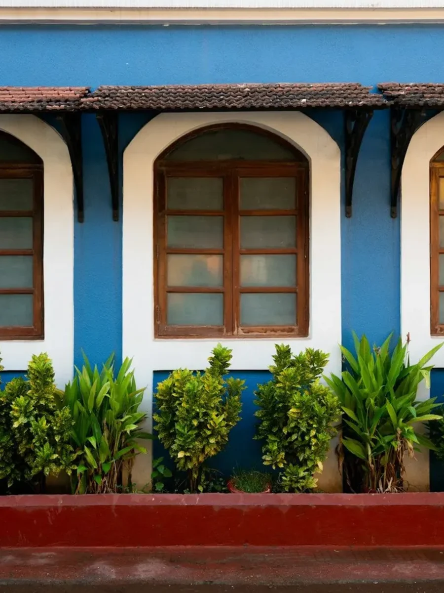 Blue house facade with three white-framed arched windows under a tiled awning on iron brackets