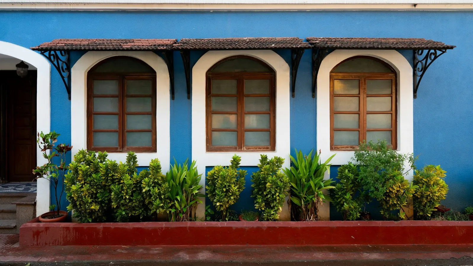 Blue house facade with three white-framed arched windows under a tiled awning on iron brackets