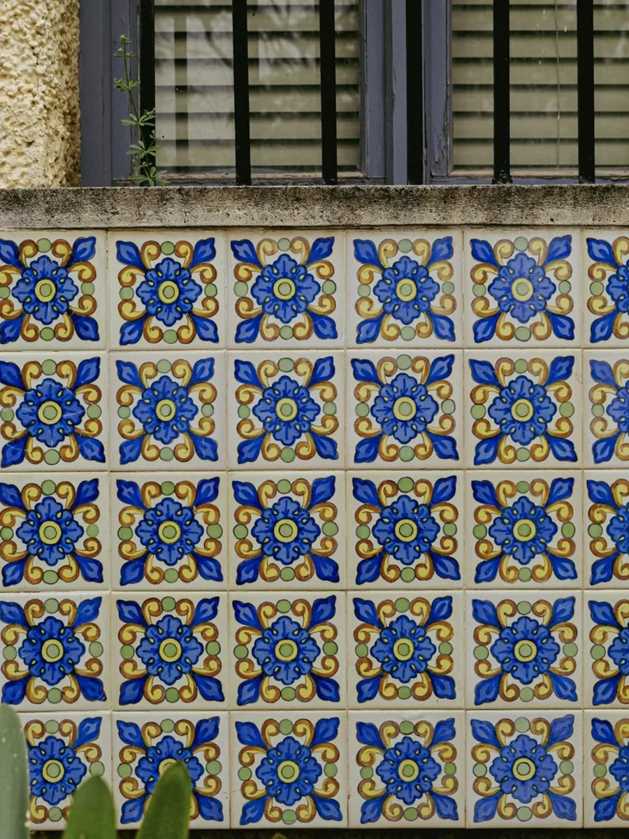 Panel of hand-painted blue and yellow ceramic tiles set into a textured wall below a window