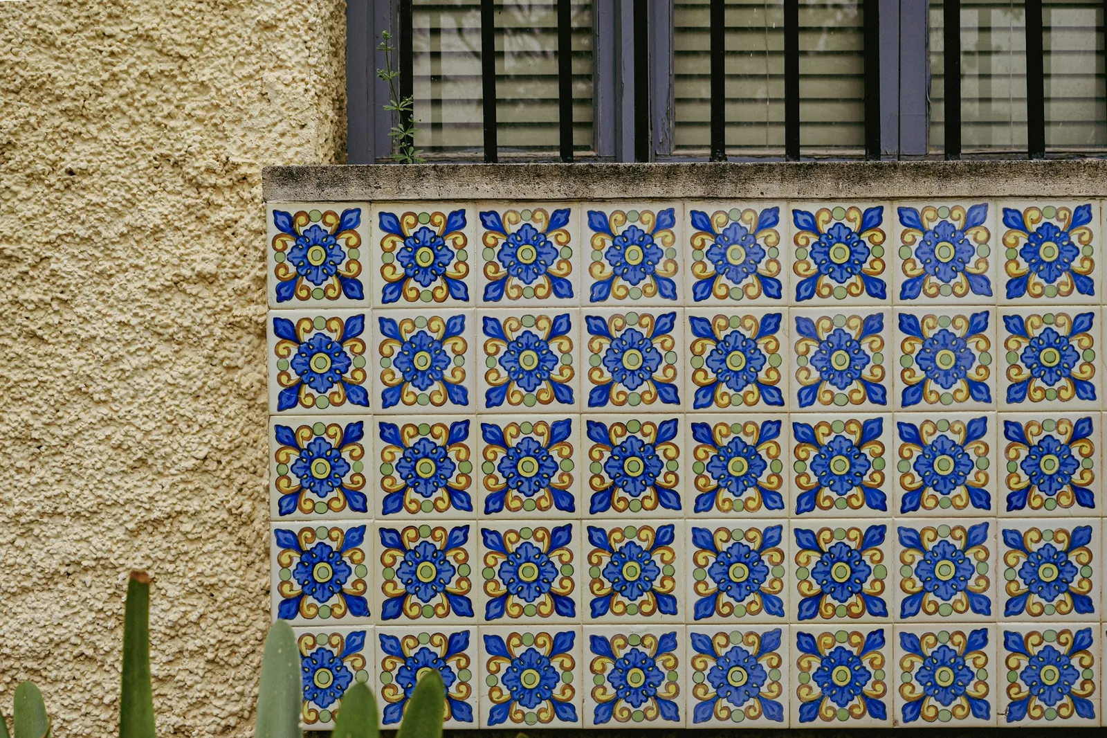 Panel of hand-painted blue and yellow ceramic tiles set into a textured wall below a window