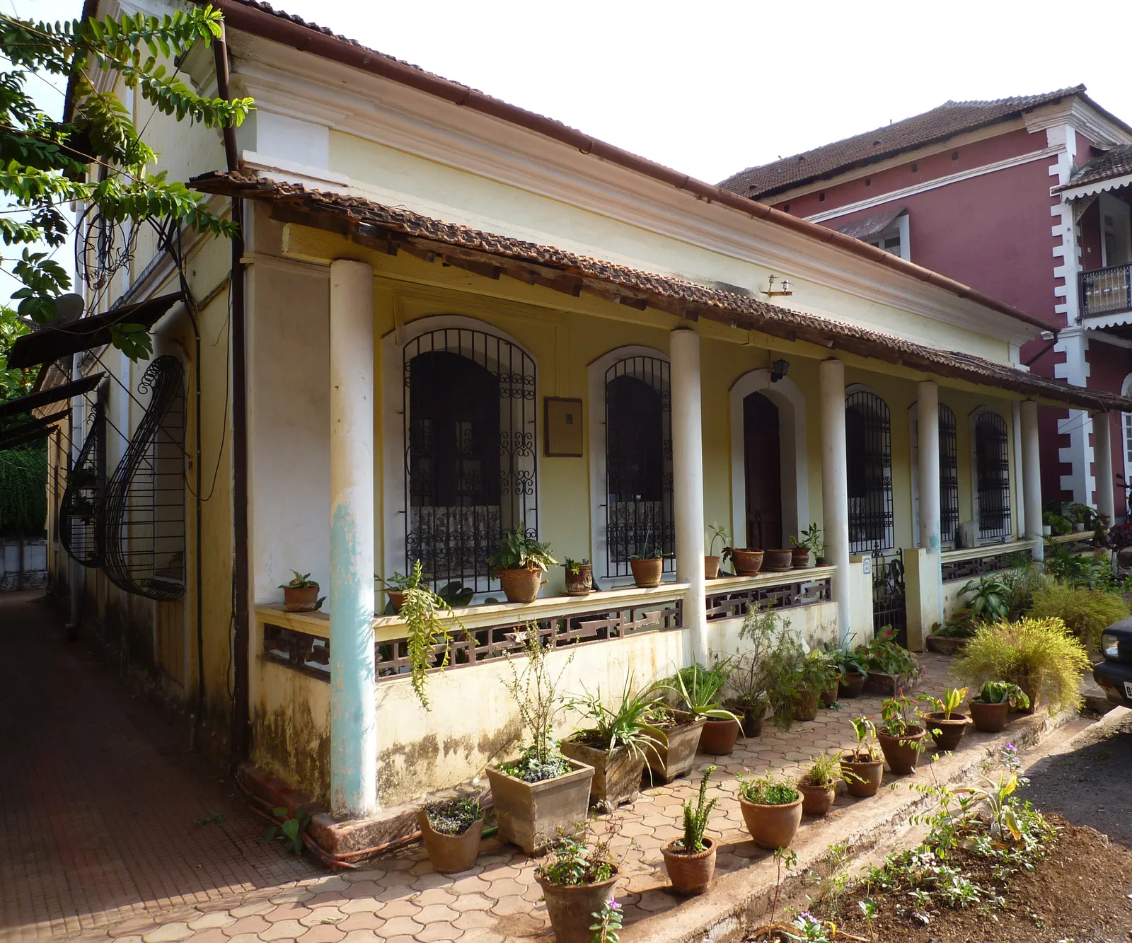 A single-storey Fontainhas house with a long verandah of round white columns, railings and potted plants